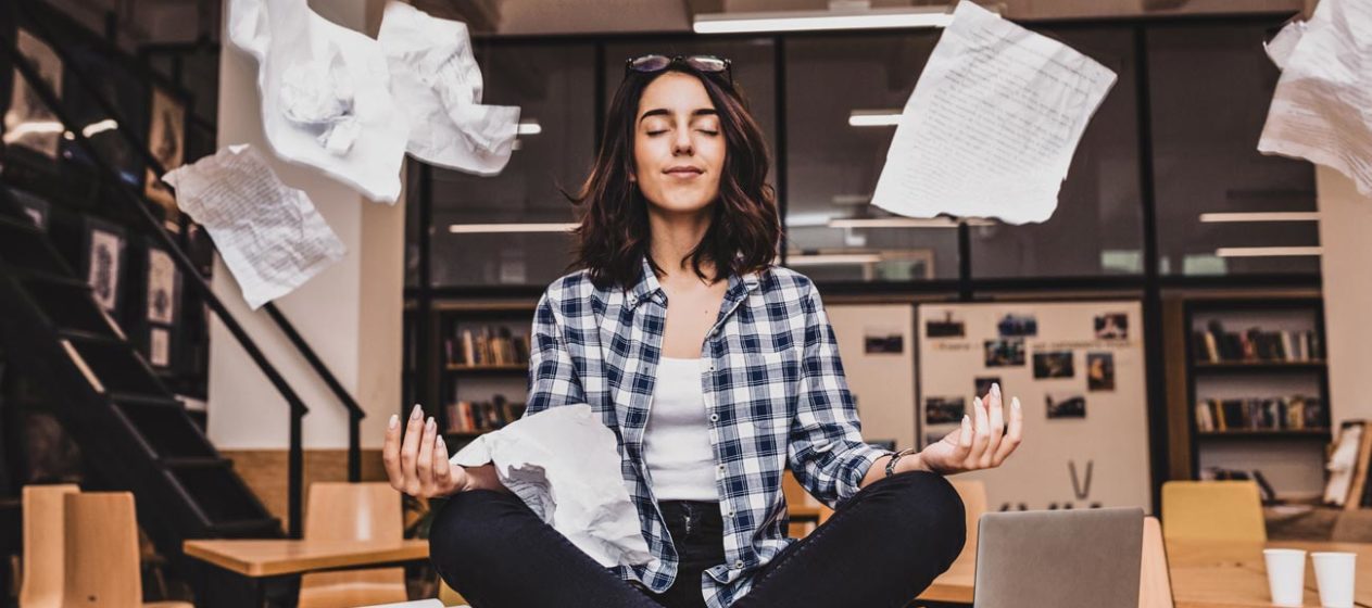 Photo of a woman meditating on a desk, surrounded by paperwork
